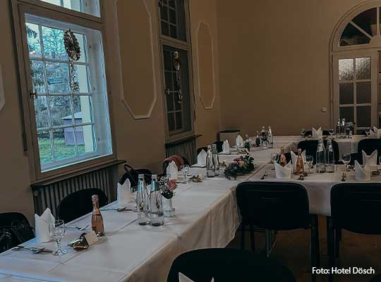 Dunkle Stühle, weiß gedeckte Tafeln und große Fenster