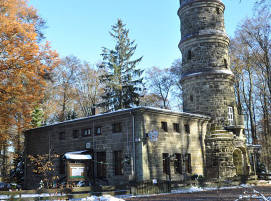 Großer Aussichtsturm mit dazugehörigem Restaurant mitten auf dem Berg im Wald.