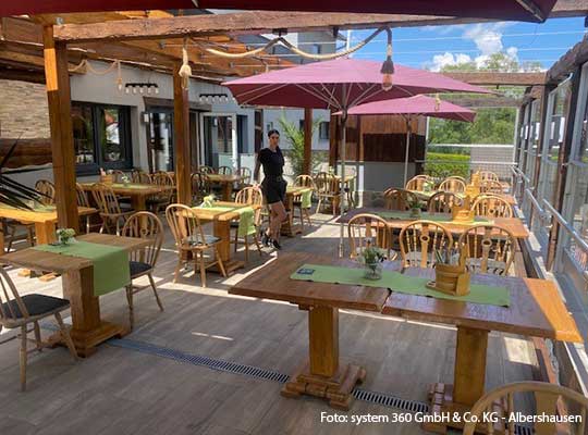 Großer schöner, sonnenbestrahlter Terrassenbereich mit vielen Sitzgelegenheiten und Sonnenschirmen.