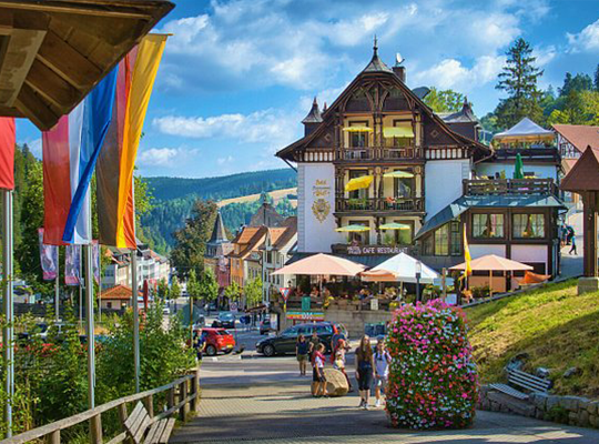 Farbenfroher Blick in das Städtchen Triberg, mit Fahnen auf der linken Seite und einem großen imposanten Haus in der Mitte.